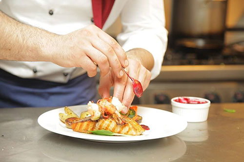 chef's hands adding sauce to a gourmet plate of food
