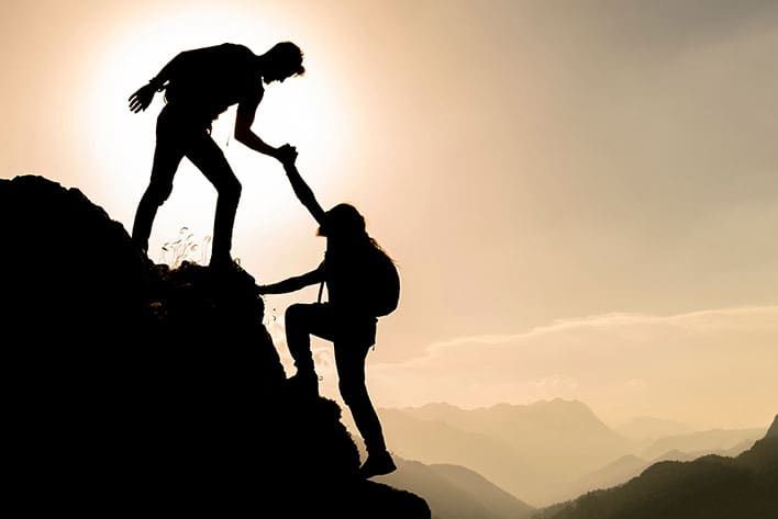 silhouette of a person helping another to climb to top of the mountain
