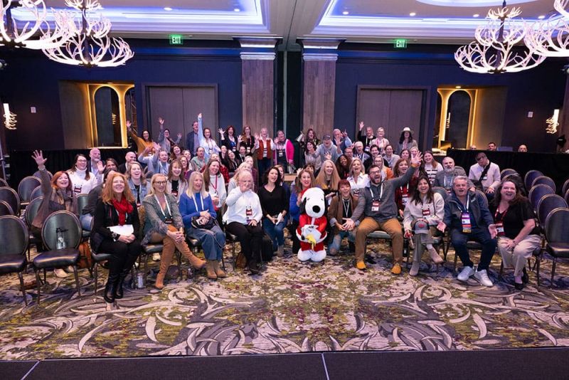 SITE Southeast members posing for a photo in a conference room with a Snoopy mascot in the center. Some are seated and others are standing, smiling at the camera.