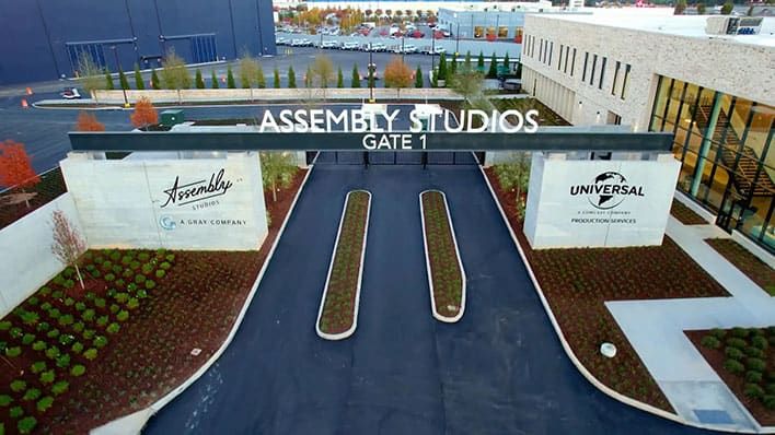 Gate 1 entrance to Assembly Studios Atlanta, with adjacent landscaped areas and visible studio logos.