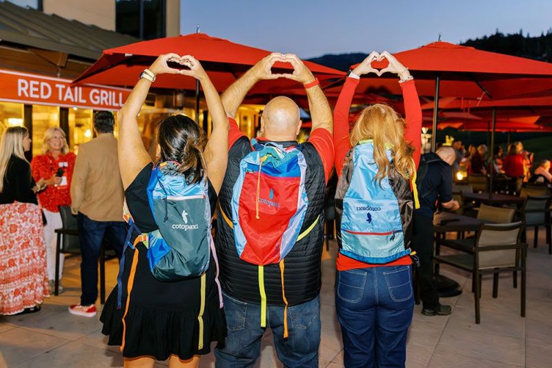 3 people wearing backpacks, their hands shaped like a heart help high over their heads